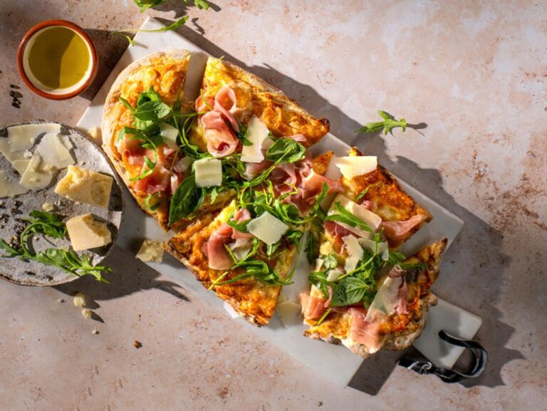 Di Parma Hand-stretched Italian sourdough pizza topped with prosciutto, rucola, fresh basil, parmesan flakes.